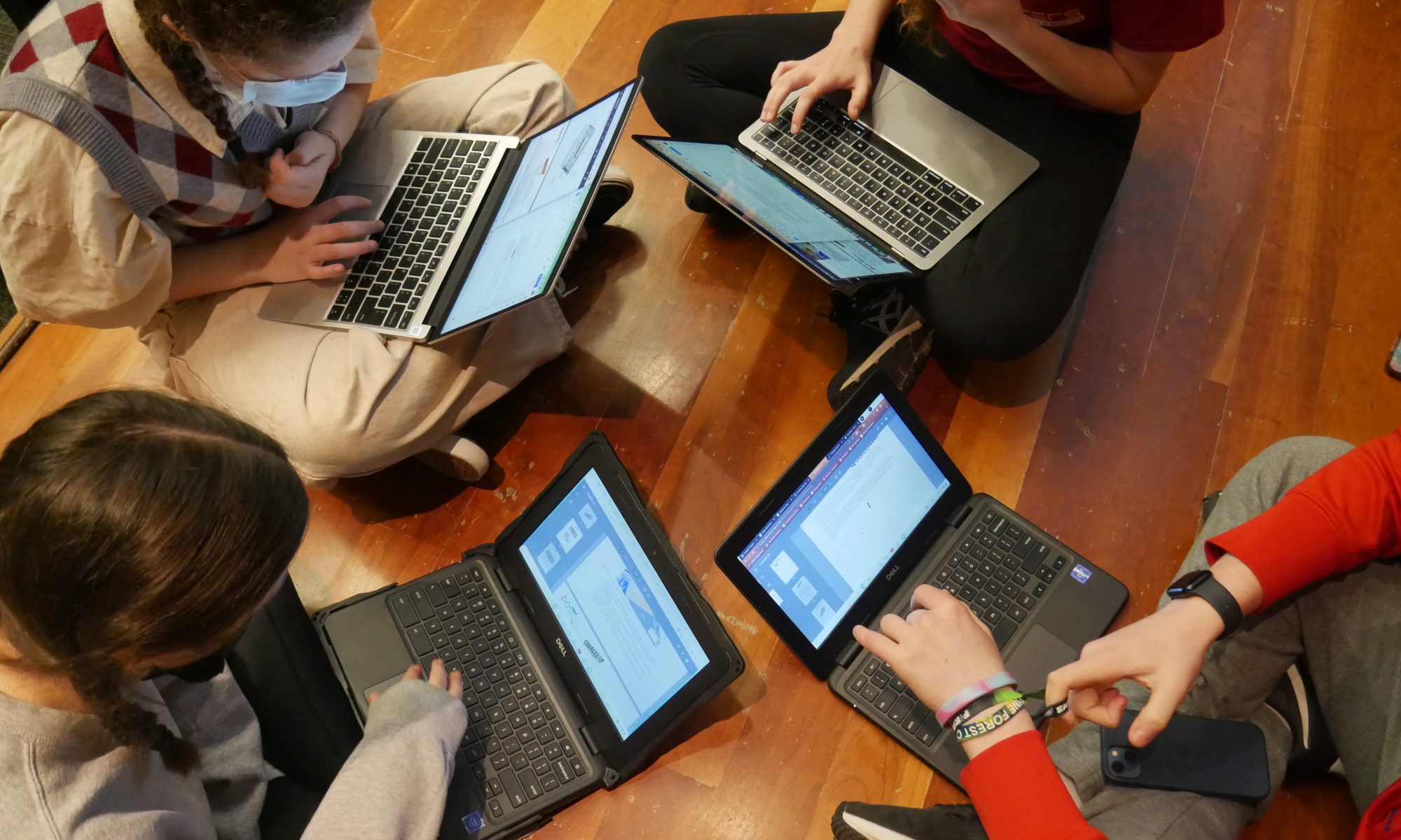An overhead view of 4 students sitting in a circle with open laptops